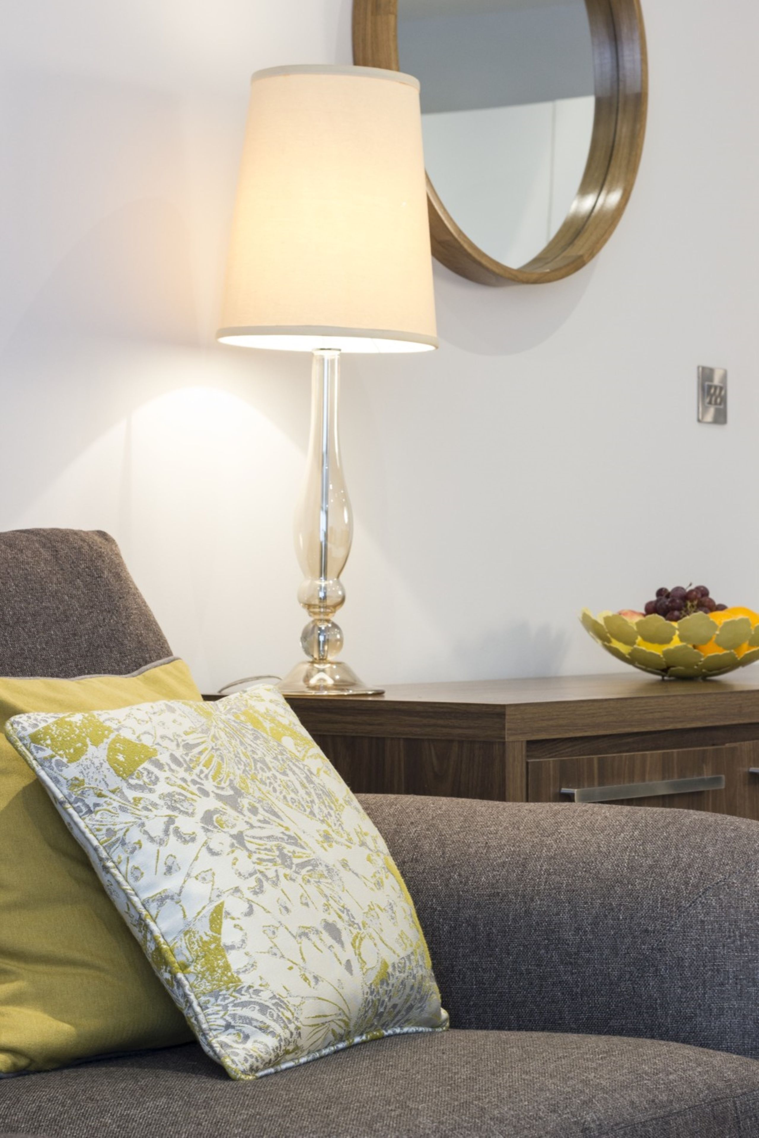 A living room with a sofa, a lamp, a mirror, and a fruit bowl.
