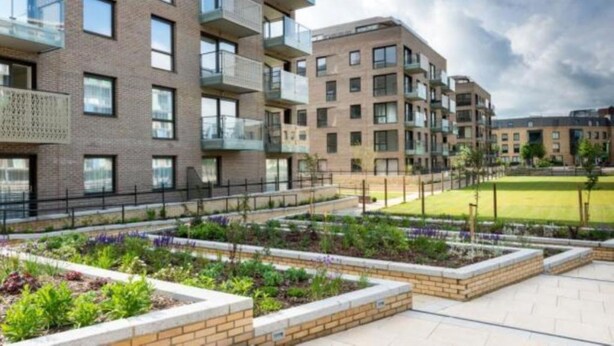 A modern apartment complex with multiple floors, balconies, and a landscaped courtyard with raised garden beds. - Citystay Living - Mill Park Apartments (Cambridge)