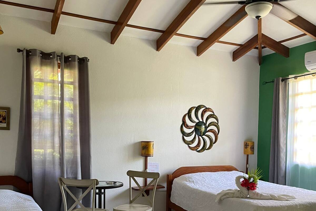 A hotel room with two beds, a small table with chairs, a ceiling fan, and a decorative wall piece.