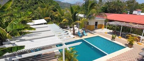 A pool area with lounge chairs and a small building, surrounded by tropical vegetation.