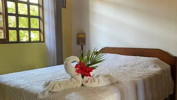 Cama bem arrumada com colcha branca e toalhas dispostas em formato de cisne decorativo.