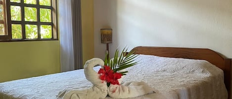 A neatly made bed with a white bedspread and a decorative swan-shaped towel arrangement.
