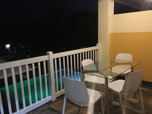 Enjoy a peaceful evening on the balcony with a glass table and comfortable seating for four, overlooking the serene pool and the night sky.