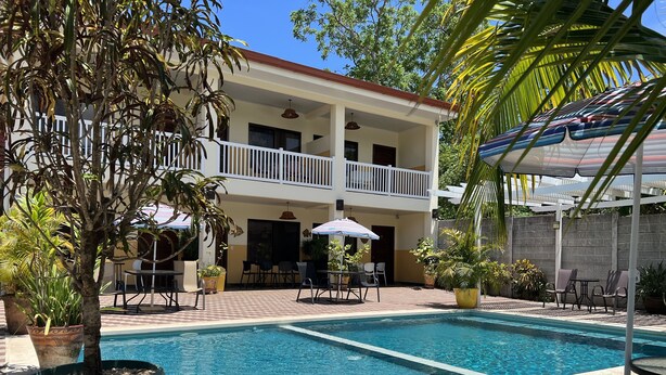 A pool area with a two-story building, outdoor seating, and potted plants. - Cabinas el Colibri (Puerto Carrillo)