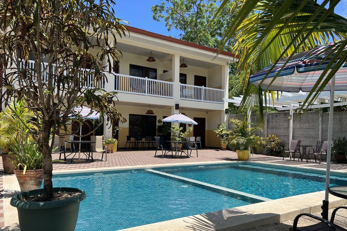 A pool area with a two-story building, outdoor seating, and potted plants.