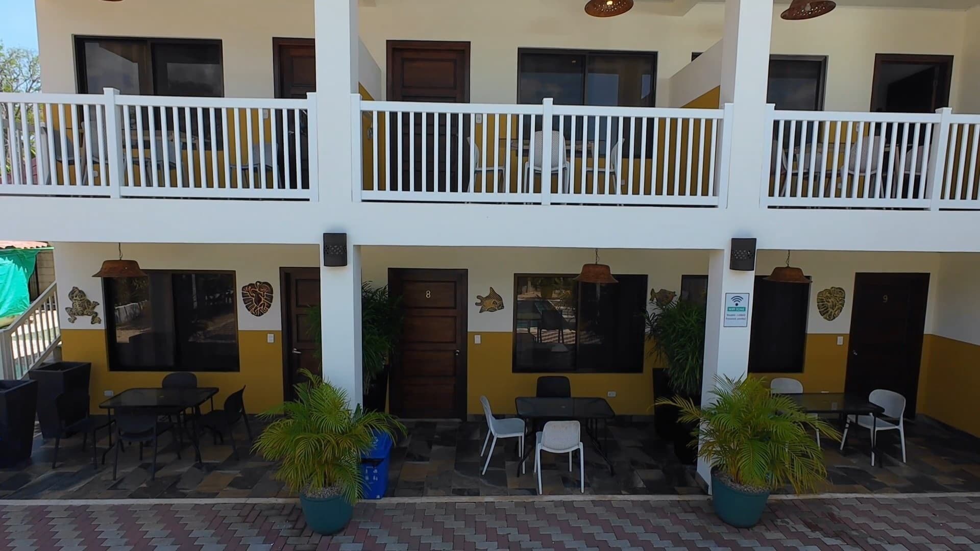A two-story building with a balcony, outdoor seating area, and potted plants.