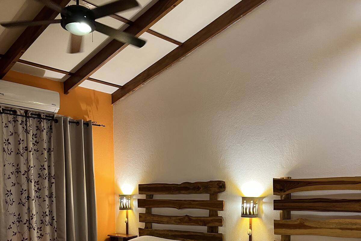 A hotel room with two beds, wooden headboards, bedside lamps, and a ceiling fan.