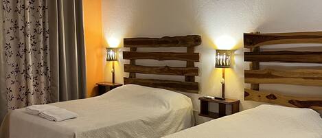 A hotel room with two beds, wooden headboards, bedside lamps, and a ceiling fan.