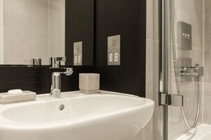 A modern bathroom with a large white sink, a glass shower enclosure, and dark wall tiles.