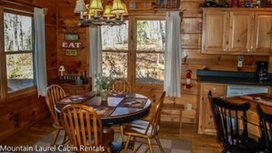 A cabin with a wooden interior, a dining table with chairs, a chandelier, and a kitchen area with cabinets.