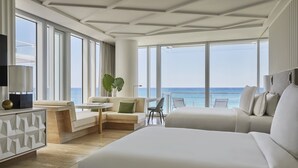 A modern hotel room with large windows, a sofa, a chair, a small table, and a decorative plant. - Four Seasons Hotel at The Surf Club (Surfside)