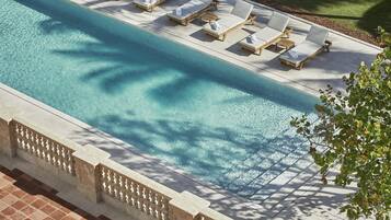 Piscina com espreguiçadeiras e um deck revestido de azulejos.