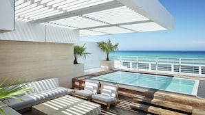A modern outdoor lounge area with a pool, seating, and a view of the ocean. - Four Seasons Hotel at The Surf Club (Surfside)
