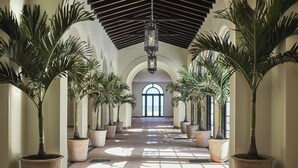 A corridor with potted plants, a tiled floor, and a large arched doorway at the end. - Four Seasons Hotel at The Surf Club (Surfside)