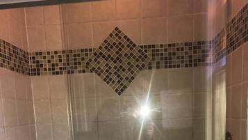 Une cabine de douche fermée par des parois en verre, avec un mur carrelé, une fenêtre et deux serviettes blanches suspendues à un porte-serviettes.