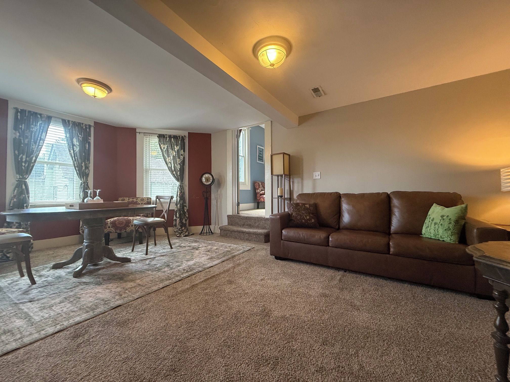 A living room with a brown leather sofa, a dining table with chairs, and a staircase leading to another level.