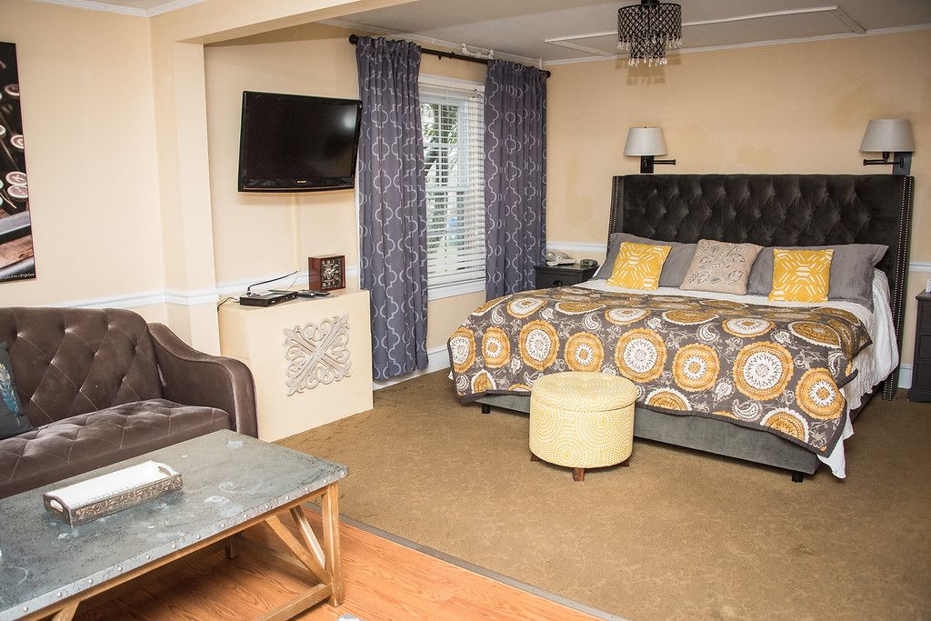 Een slaapkamer met een groot bed, een aan de muur bevestigde televisie en een raam met gordijnen.