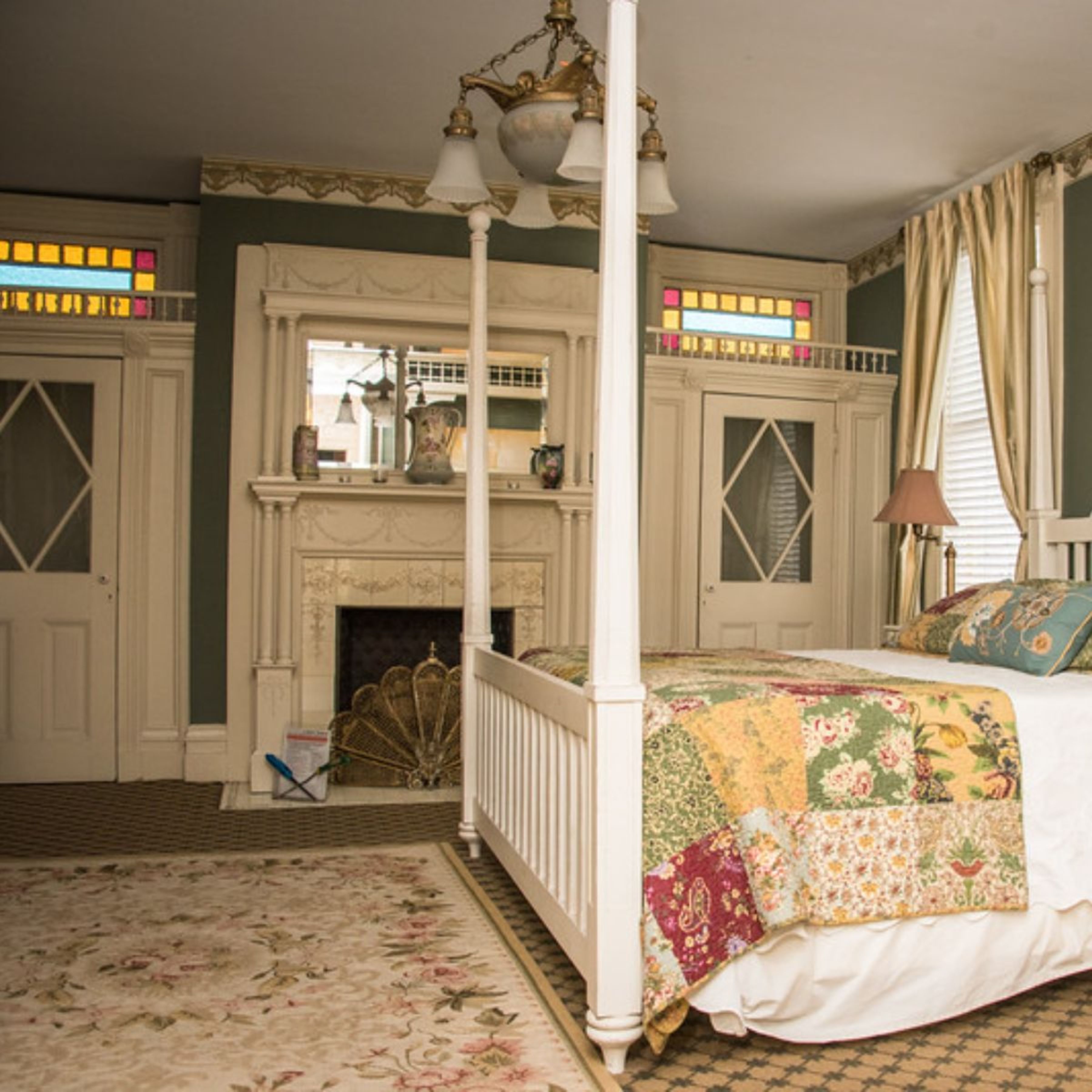 A bedroom with a four-poster bed, a fireplace, and a stained glass window.