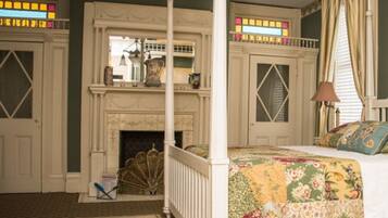 A bedroom with a four-poster bed, a fireplace, and a stained glass window.