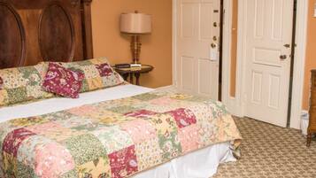 A bedroom with a large bed, a wooden headboard, a bedside table with a lamp, and two white doors.