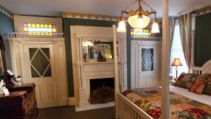 A bedroom with a four-poster bed, a fireplace, a mirror, and a stained glass window. - Vandiver Inn (Havre De Grace)