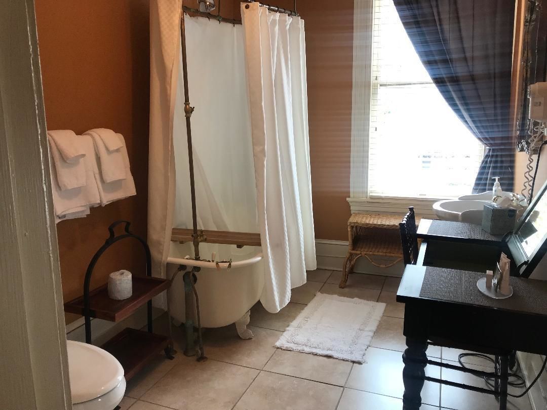 Een badkamer met een bad, toilet, wastafel en een raam met gordijnen.