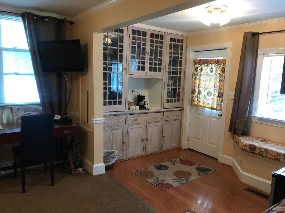 A compact kitchen with wooden cabinets, a built-in coffee maker, and a window with floral curtains.
