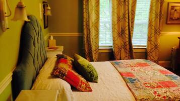 A bedroom with a bed, pillows, a nightstand, a lamp, and curtains.