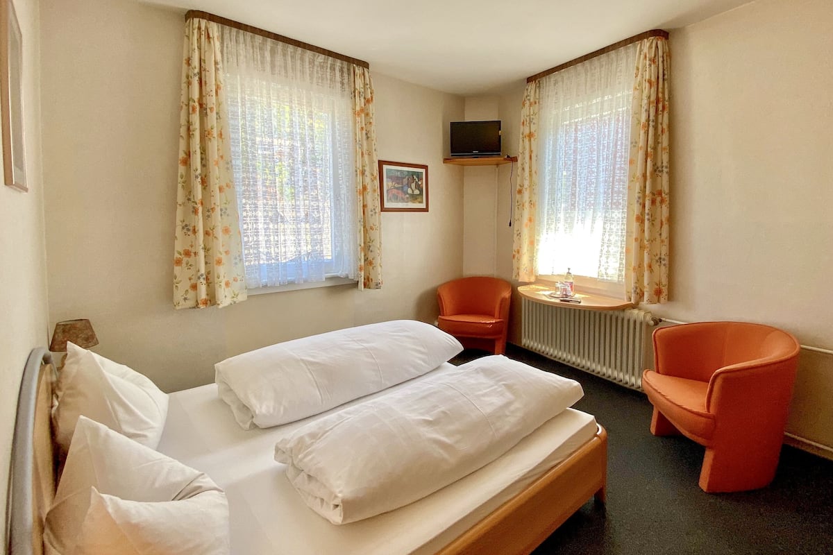 A hotel room with a bed, two chairs, a small table, and a TV on a stand.