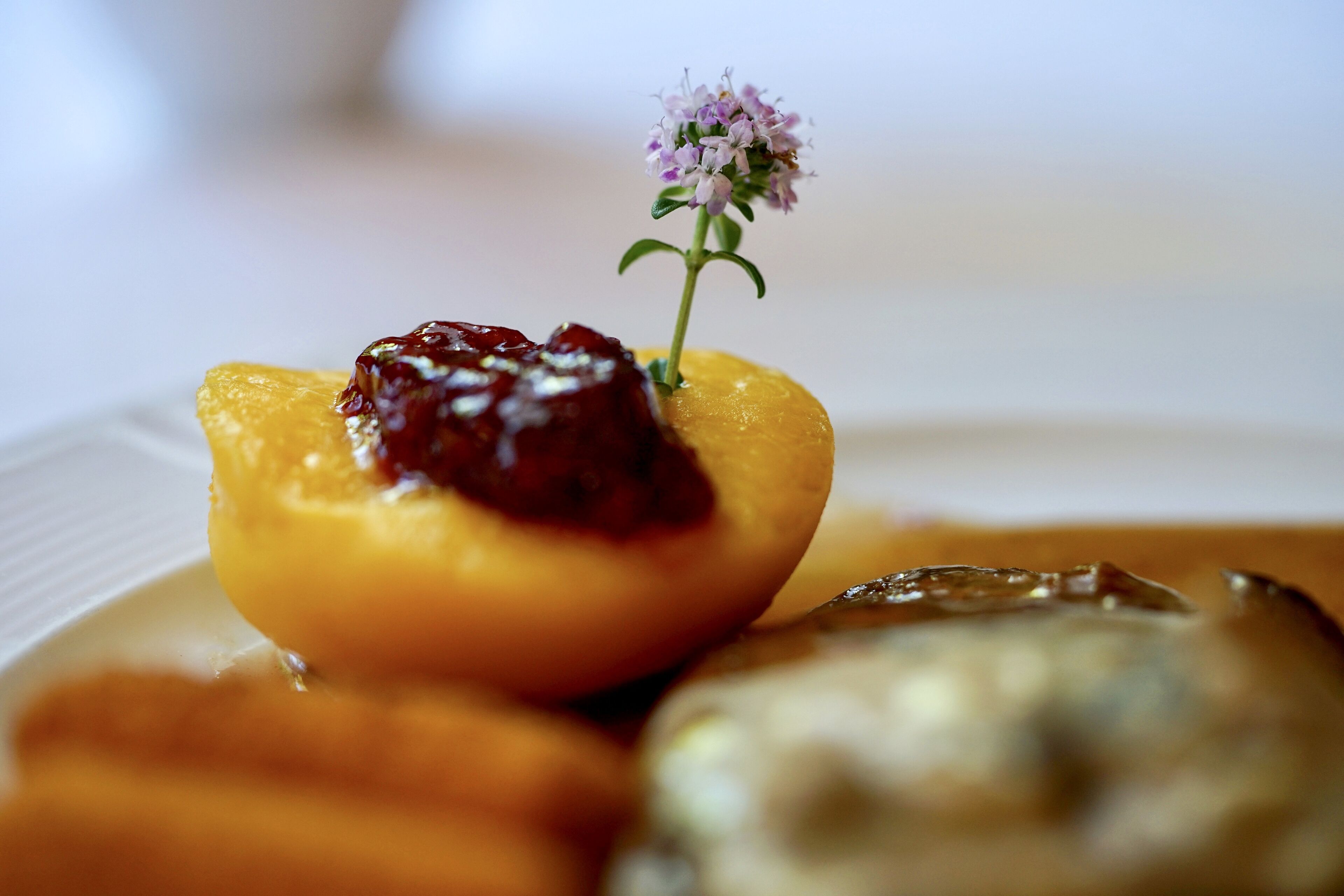 A dessert plate with a peach-shaped pastry topped with a red sauce and a small purple flower.