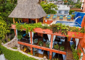 Un hotel con piscina, mobiliario exterior y abundante vegetación.