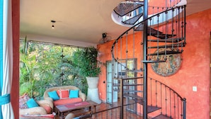 A spiral staircase with a metal railing, a wicker sofa with colorful cushions, and a potted plant in the background. - Villa Lola - an Adults Only Bed & Breakfast (Puerto Vallarta)