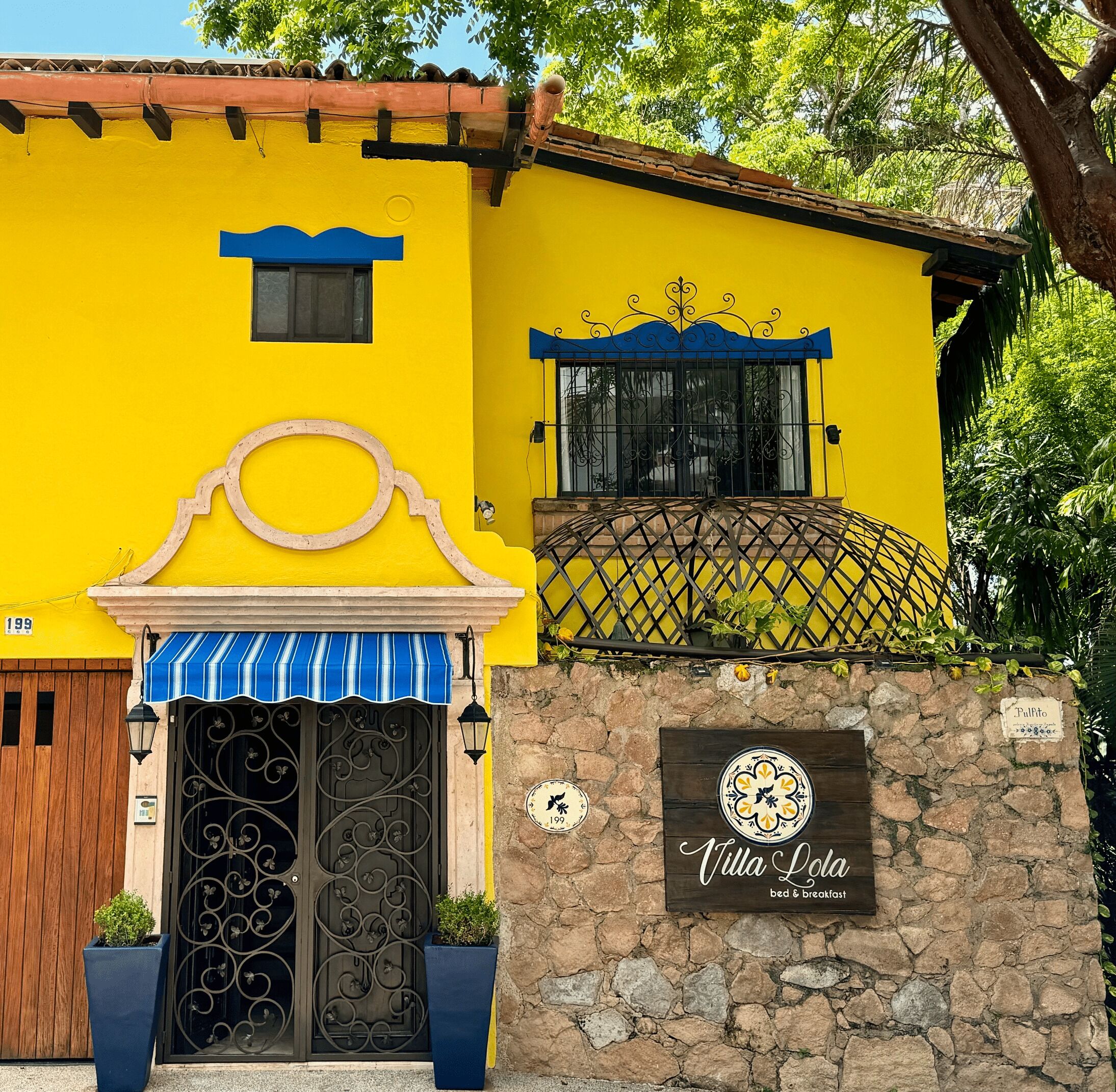 A yellow building with a stone wall, a wooden door, and a sign for Villa Lola bed & breakfast.