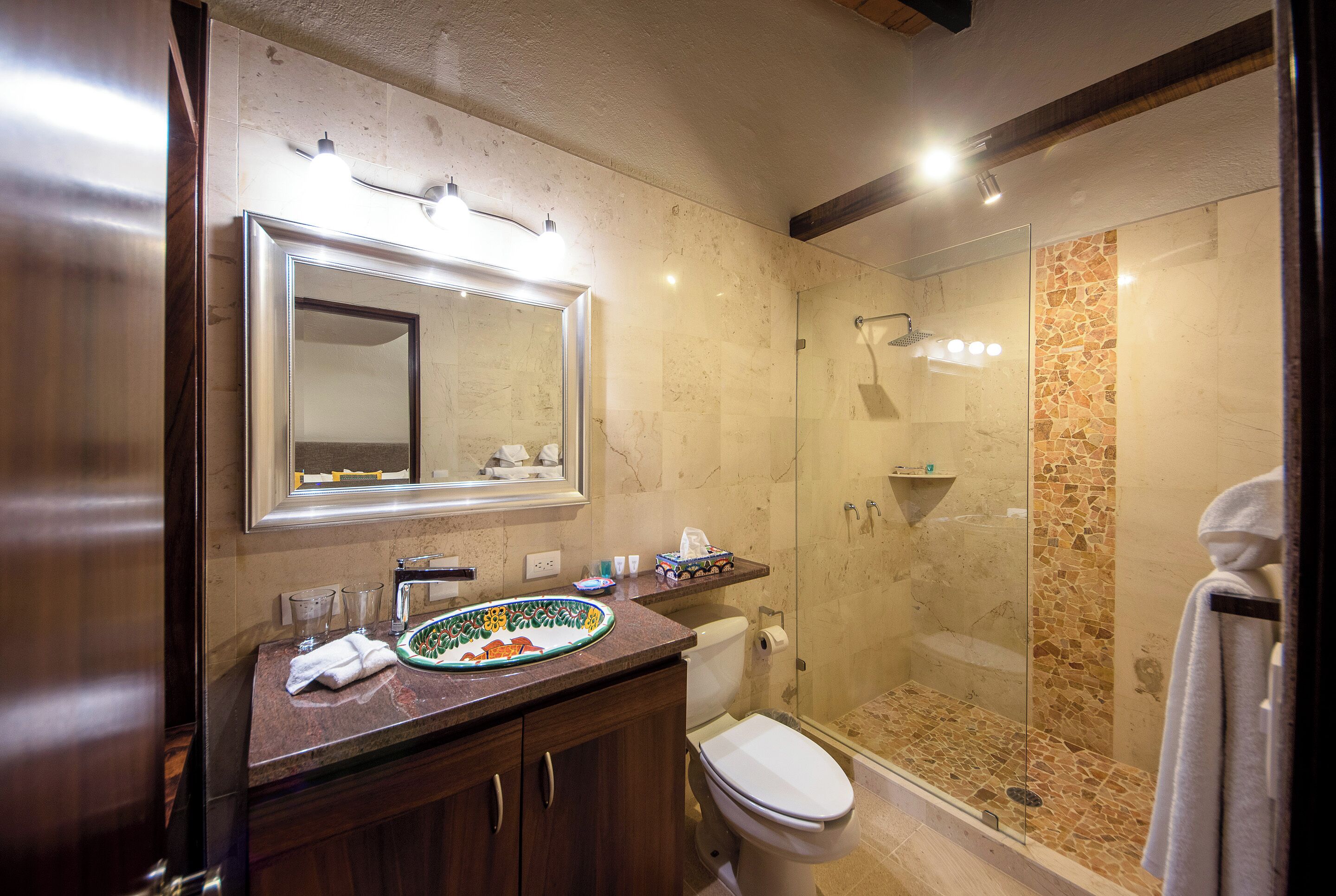 Een badkamer met een marmeren wastafel, toilet, douchecabine van glas en een spiegel boven de wastafel.