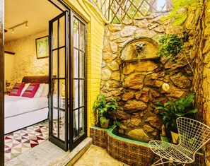 A room with a bed, a stone wall with a lion head sculpture, and a chair. - Villa Lola - an Adults Only Bed & Breakfast (Puerto Vallarta)