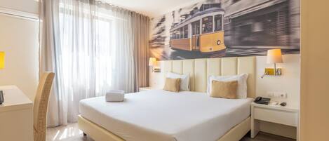 A hotel room with a large bed, a desk, a chair, a nightstand with a lamp, and a wall mural.