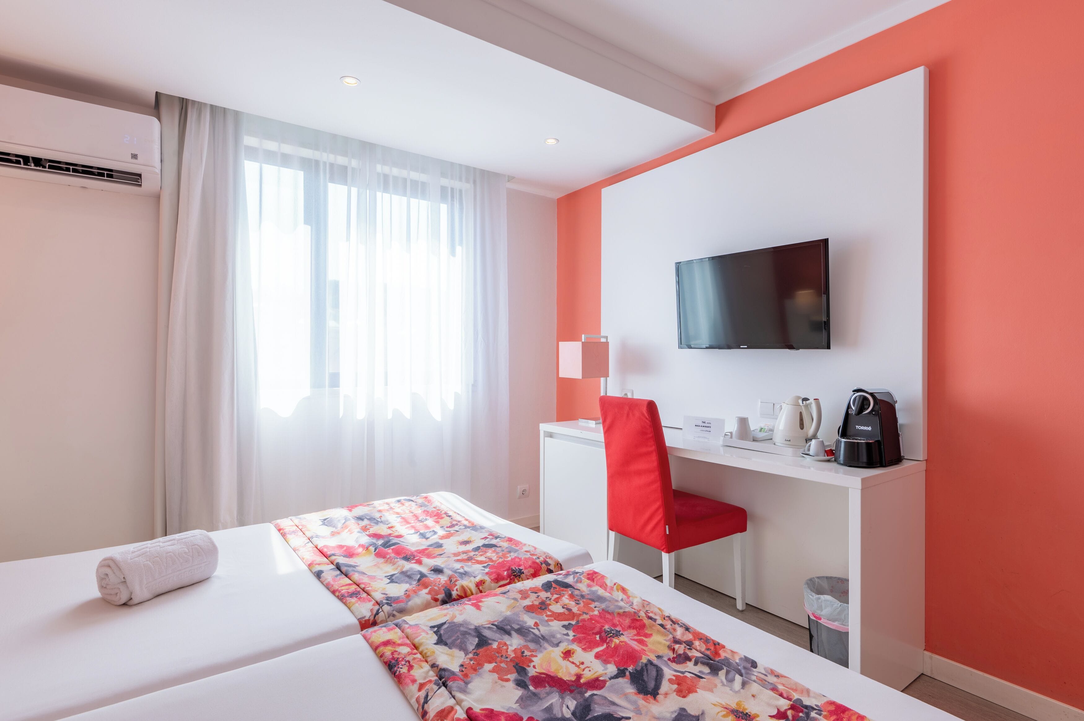 Habitación de hotel con dos camas, un escritorio, un televisor y una silla roja.