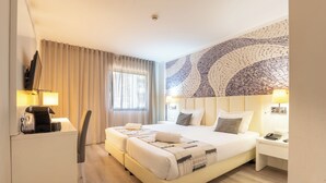 Une chambre d’hôtel avec un lit double, des tables de chevet avec des lampes, un bureau, une chaise et un grand mur décoré de mosaïques.