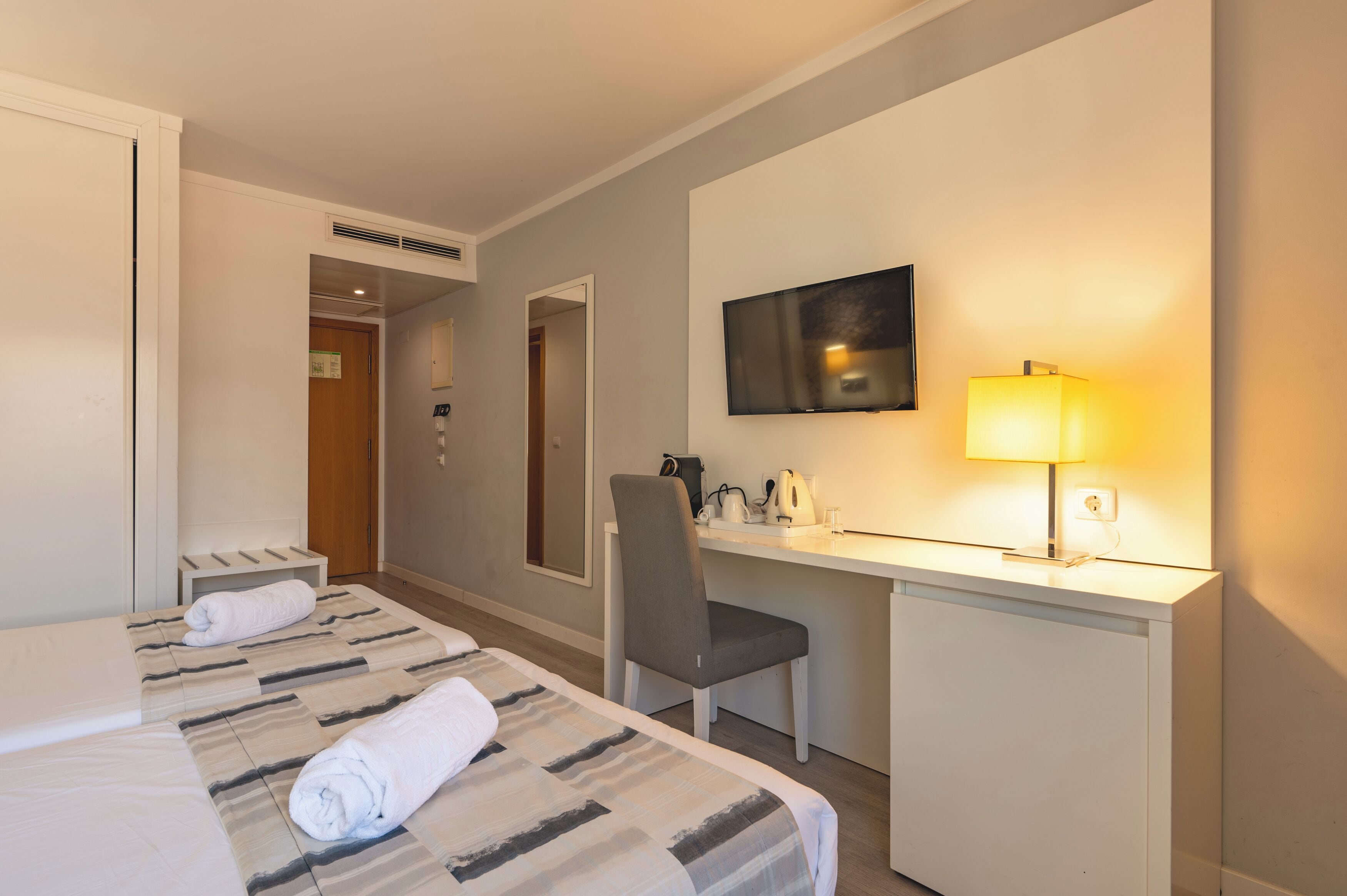 A hotel room with a bed, a desk, a chair, a TV, and a lamp.