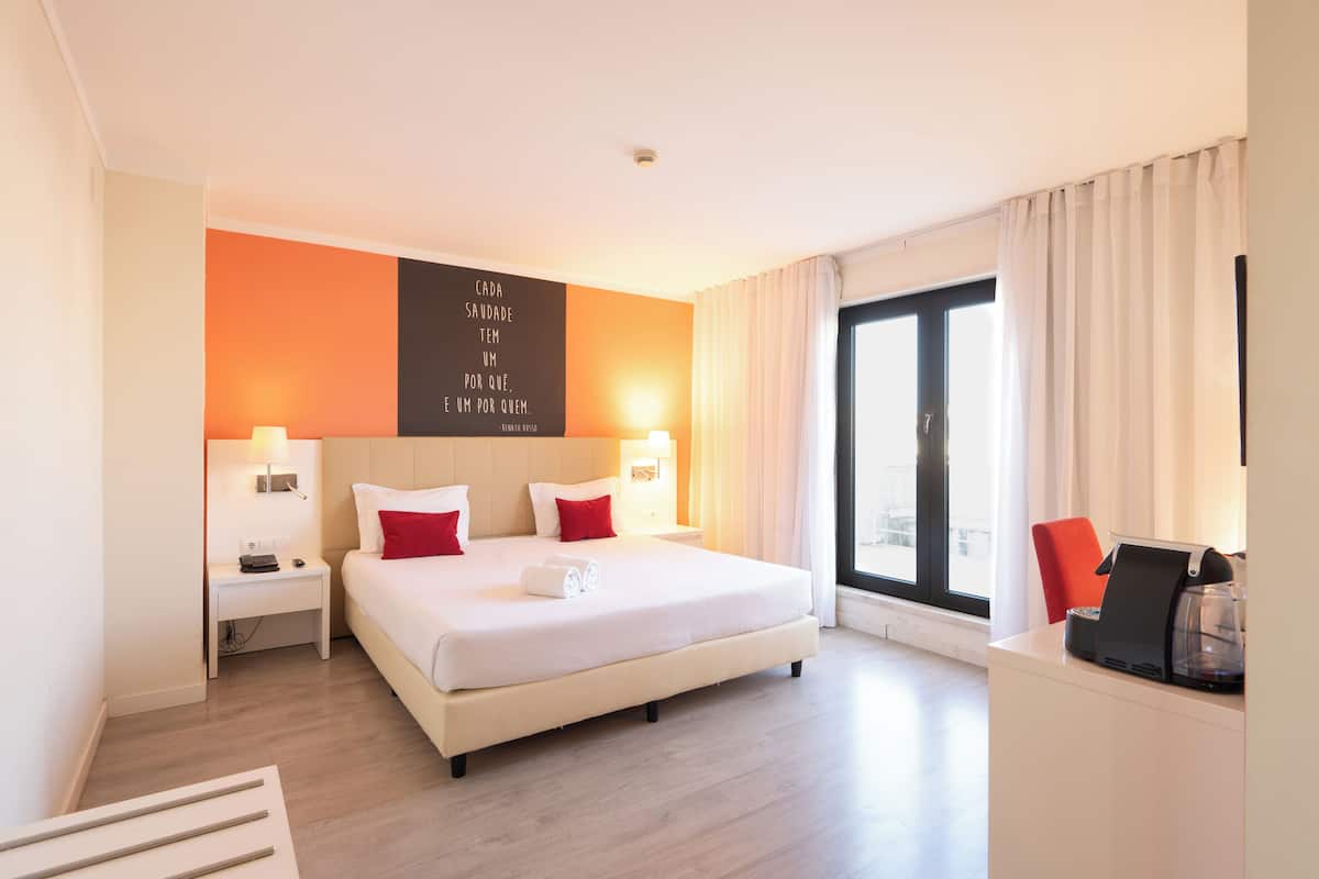 Een hotelkamer met een groot bed, twee nachtkastjes, een koffiezetapparaat en uitzicht op de stad.