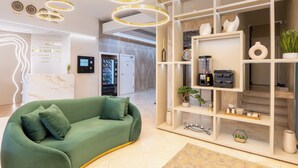 Un hall d’hôtel moderne avec un canapé vert, un comptoir d’accueil, un mini-bar et un téléviseur fixé au mur.