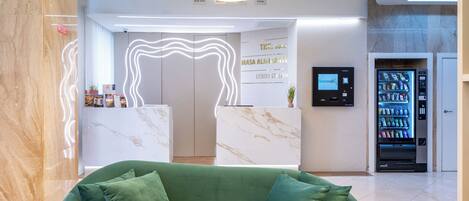 A modern lobby with a green sofa, a reception desk, a vending machine, and a marble floor.