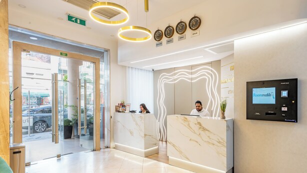 Un espace d’accueil d’hôtel avec des comptoirs en marbre, un écran numérique et une entrée avec une porte en verre.
