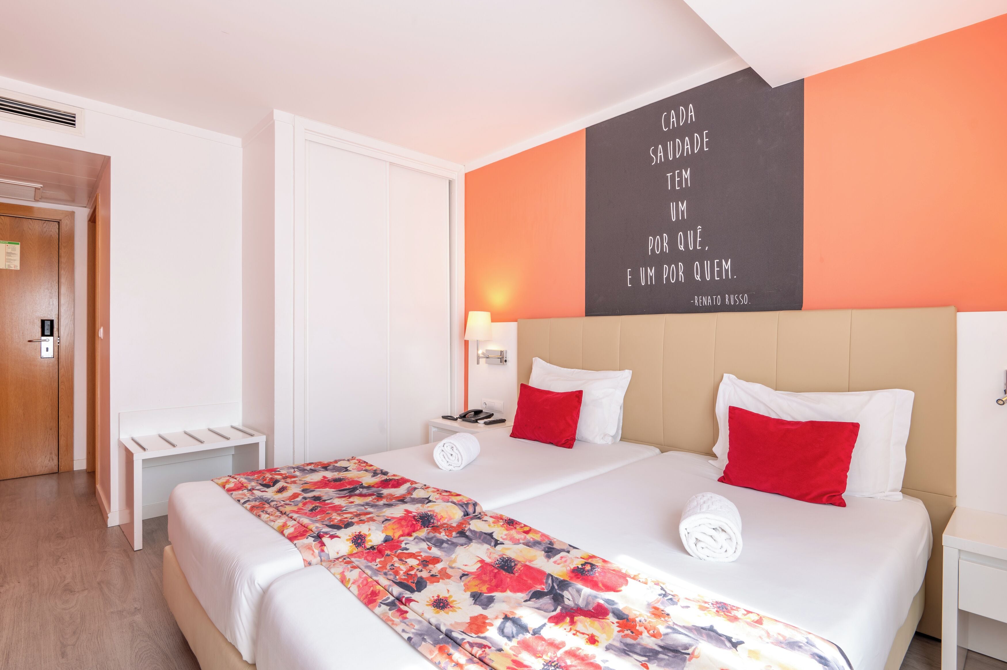 Een hotelkamer met twee bedden, een muisbriefje, een nachtkastje met een lamp en een houten deur.