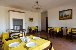 Un comedor con manteles amarillos, sillas de madera y un cuadro en la pared.