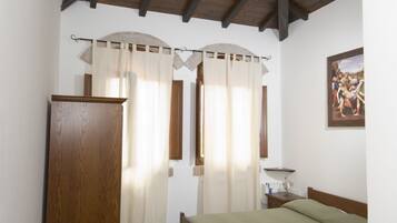 Une chambre avec un plafond en bois, un lit recouvert d’une couverture verte, une armoire en bois et une fenêtre avec des rideaux.