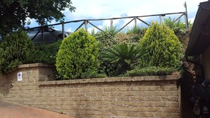 Un mur de briques sur lequel est apposé un panneau interdisant le stationnement, une clôture en métal et divers arbustes et arbres verts.
