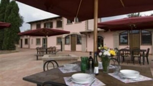 Un espace extérieur aménagé pour les repas, avec des tables, des chaises, des parasols et un bâtiment en arrière-plan.