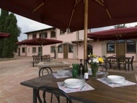 An outdoor dining area with tables and chairs, umbrellas, and a building in the background.