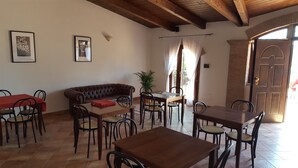 Un coin repas avec un canapé en cuir marron, des tables et des chaises en bois. Deux tableaux encadrés ornent le mur, et une plante en pot est posée à proximité.
